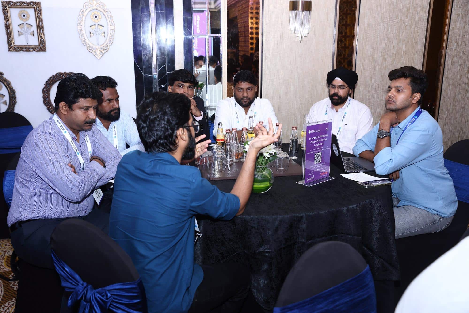 A group of seven men are in discussion, seated at a round table.